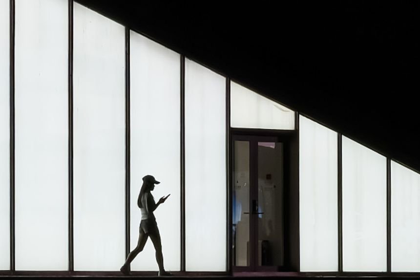 A woman walks with a smartphone in front of an illuminated wall in Shenzhen, China, April 27, 2026.