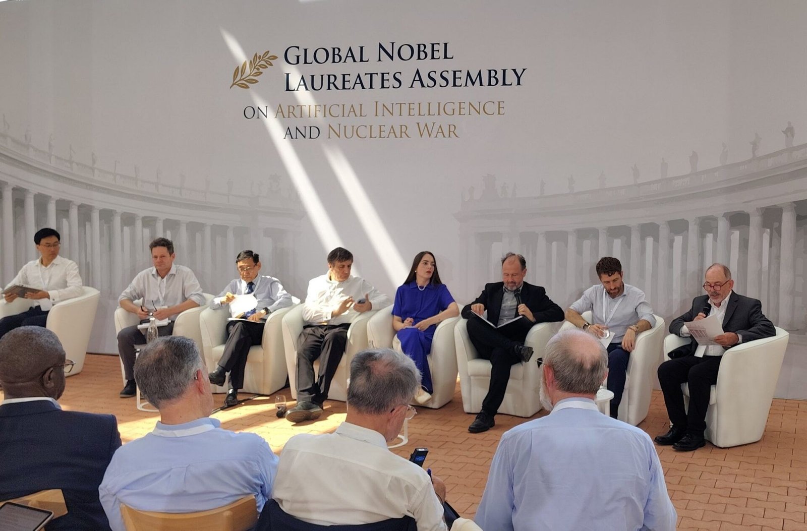 Panelists sit on stage at the Global Nobel Laureates Assembly on Artificial Intelligence and Nuclear War and speak to an audience in a bright, formal setting.