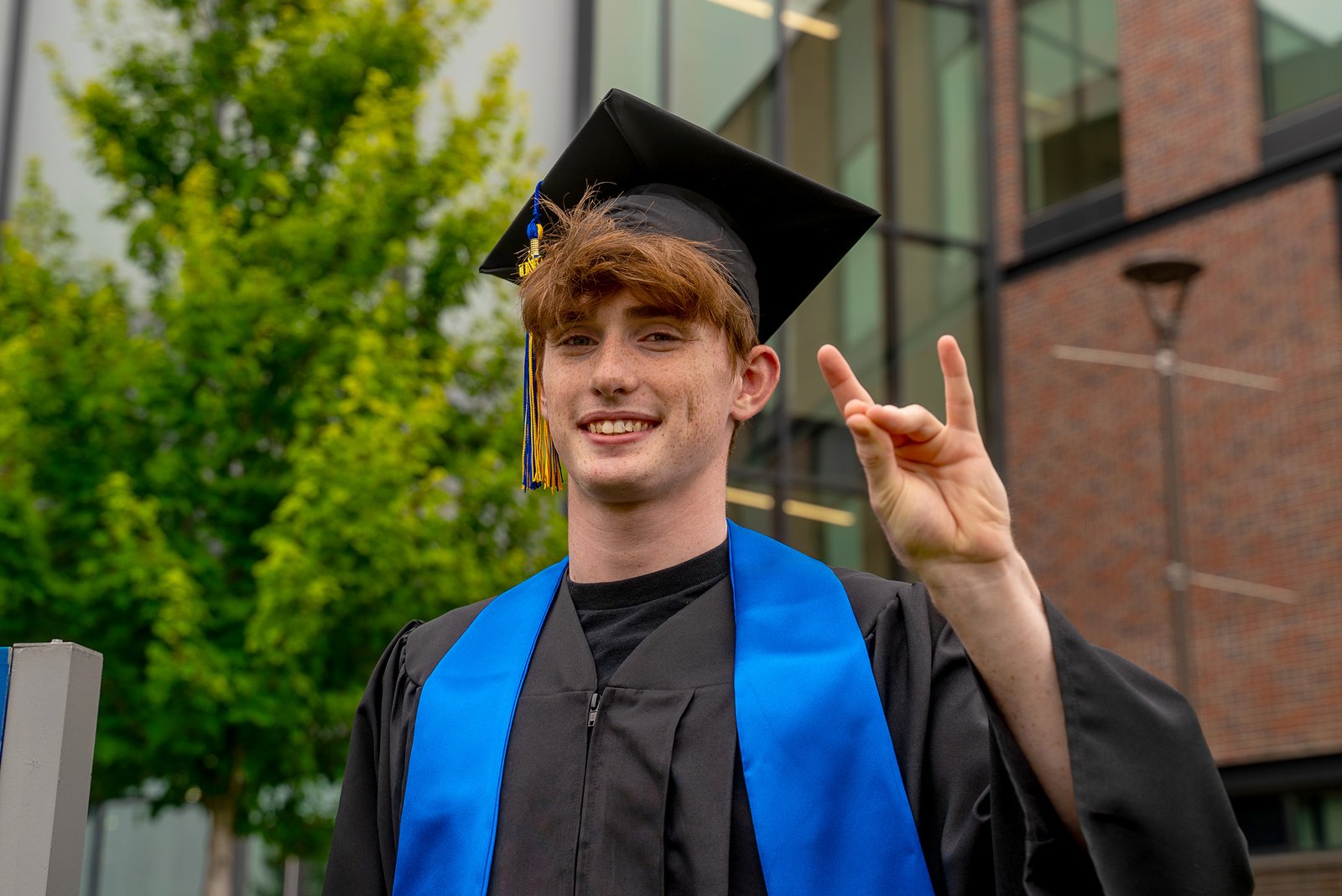 Thomas Safago poses for a photo in front of Discovery Hall in his graduation cap and gown.
