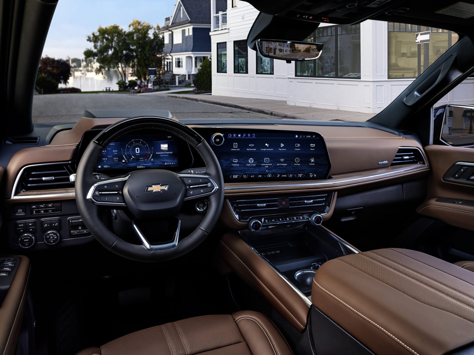 Interior of a Chevrolet vehicle with a view out the front window of houses and storefronts on a quiet street. 