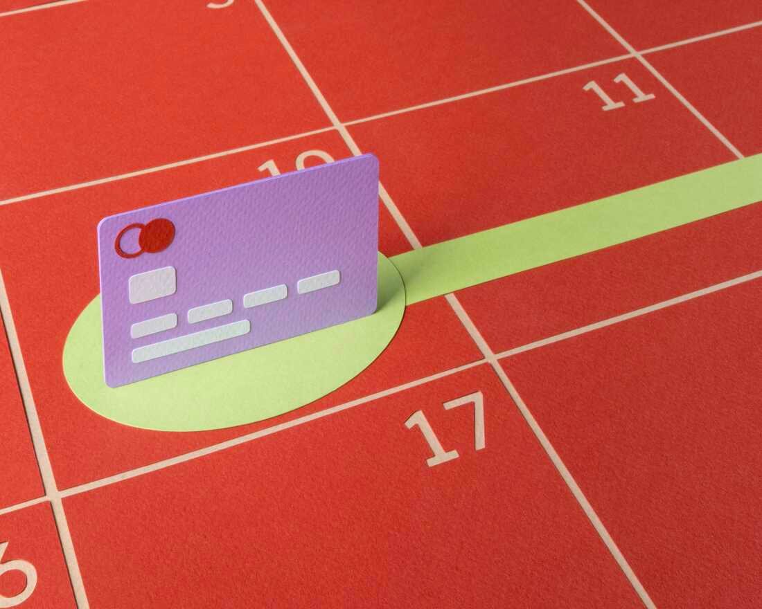 A cut paper illustration shows a purple credit card standing on a flat red calendar with numbered dates in the grid. A green circle under the card turns into a line that extends into the future, showing that you are making a plan to pay off credit card debt. 