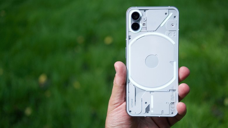 Close-up of a person holding Nothing Phone (1) with blurred grass in the background