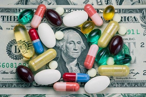 Pills of various sizes, shapes and colors arranged on a dollar bill around the portrait of George Washington in the center.