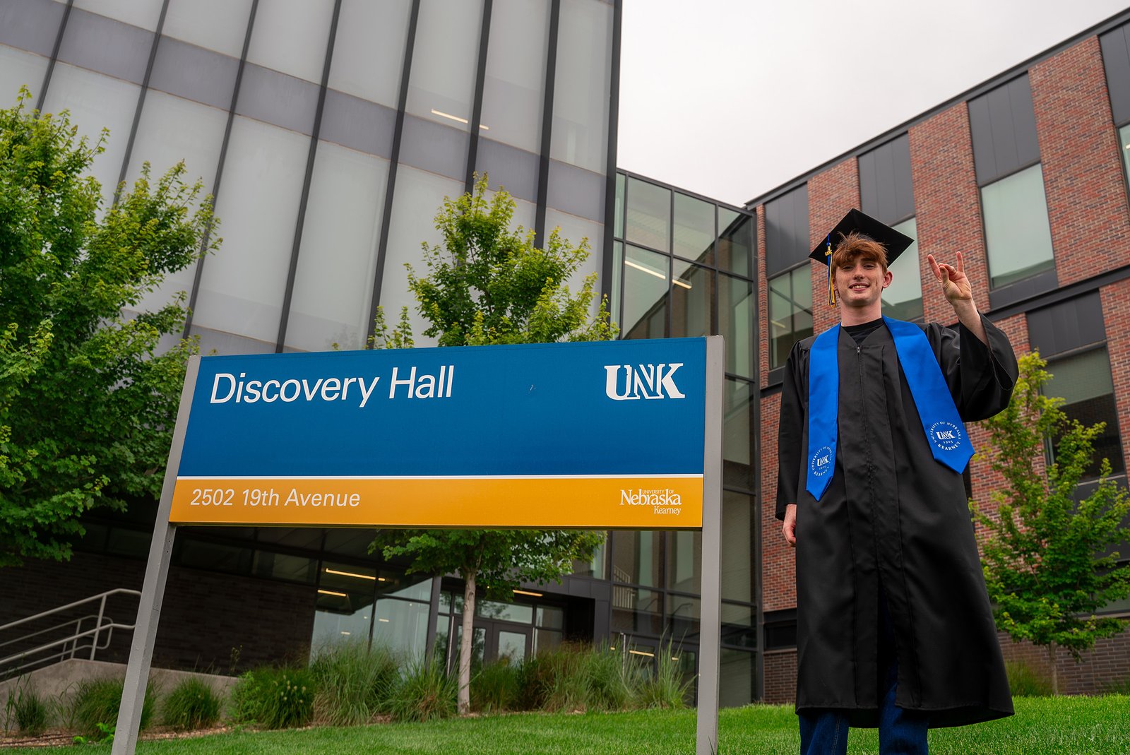Thomas Safago poses for a photo in front of Discovery Hall in his graduation cap and gown.
