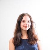 Girl with brown hair and blue shirt smiling against a plain white background